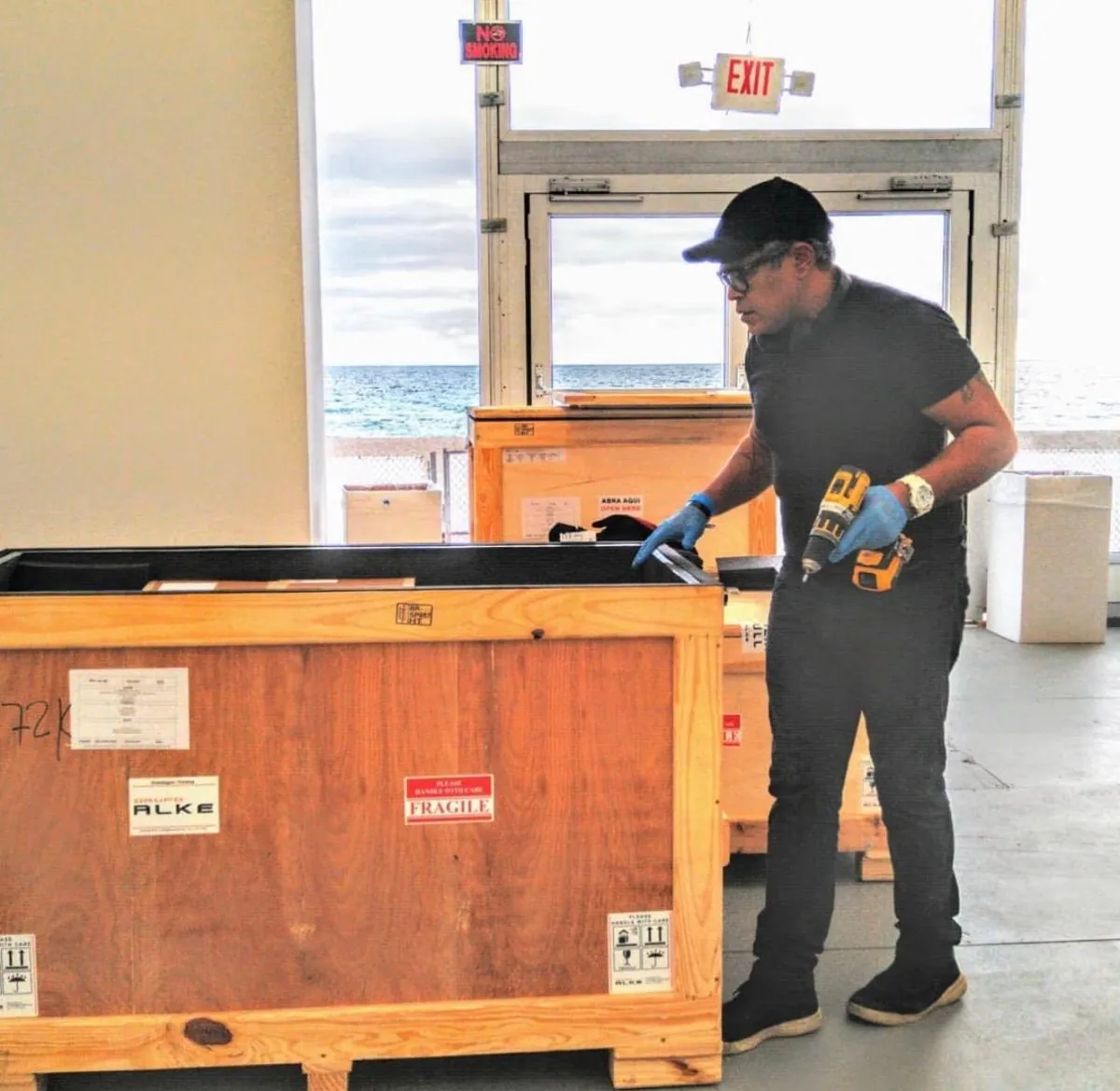 Técnico da Install com luva abrindo caixa de madeira marcada como frágil e de manuseio cuidadoso, com ferramenta própria, na UNTITLED Art, em Miami